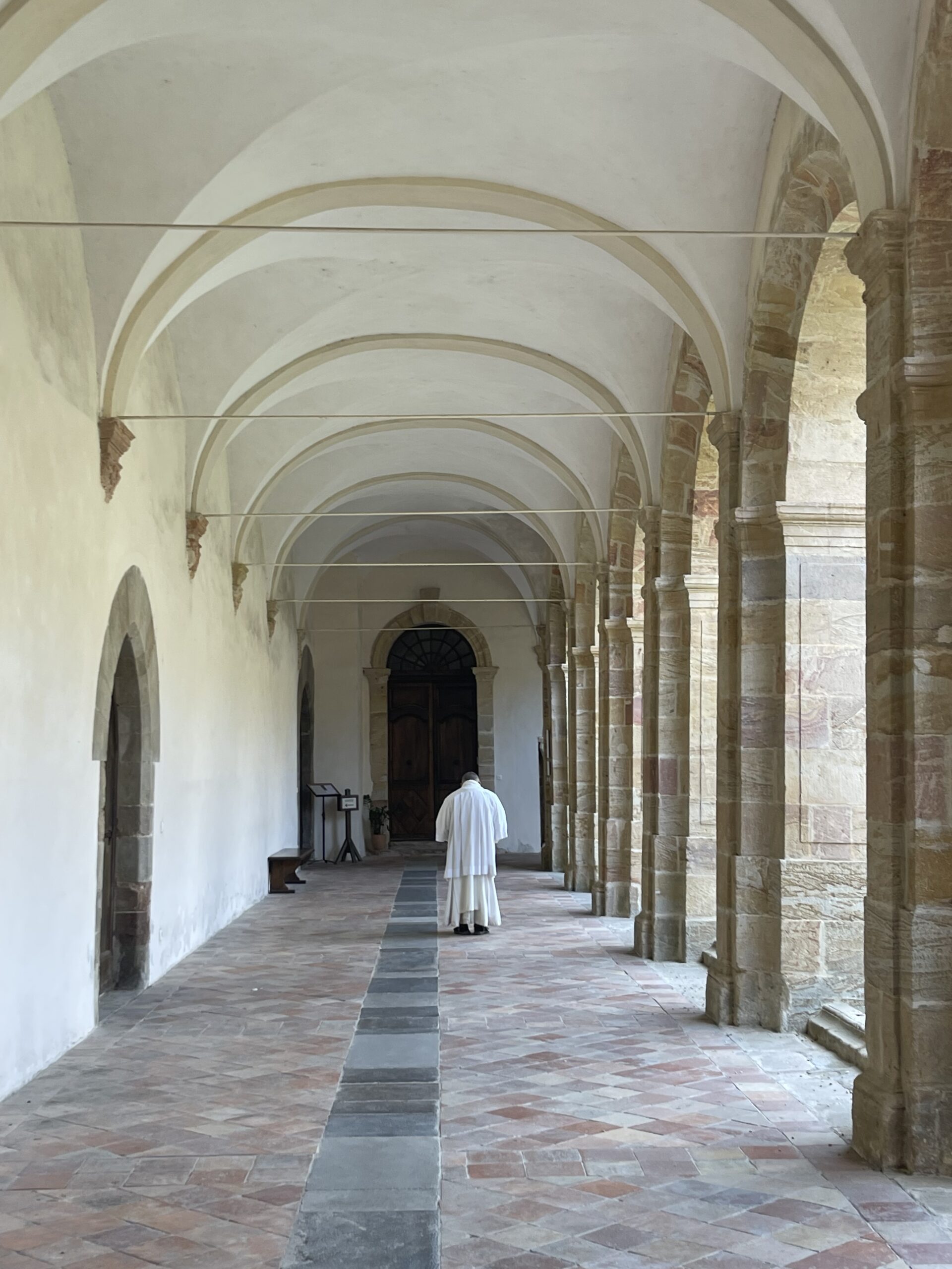 Priest in white cassock heading to Mass down corridor
