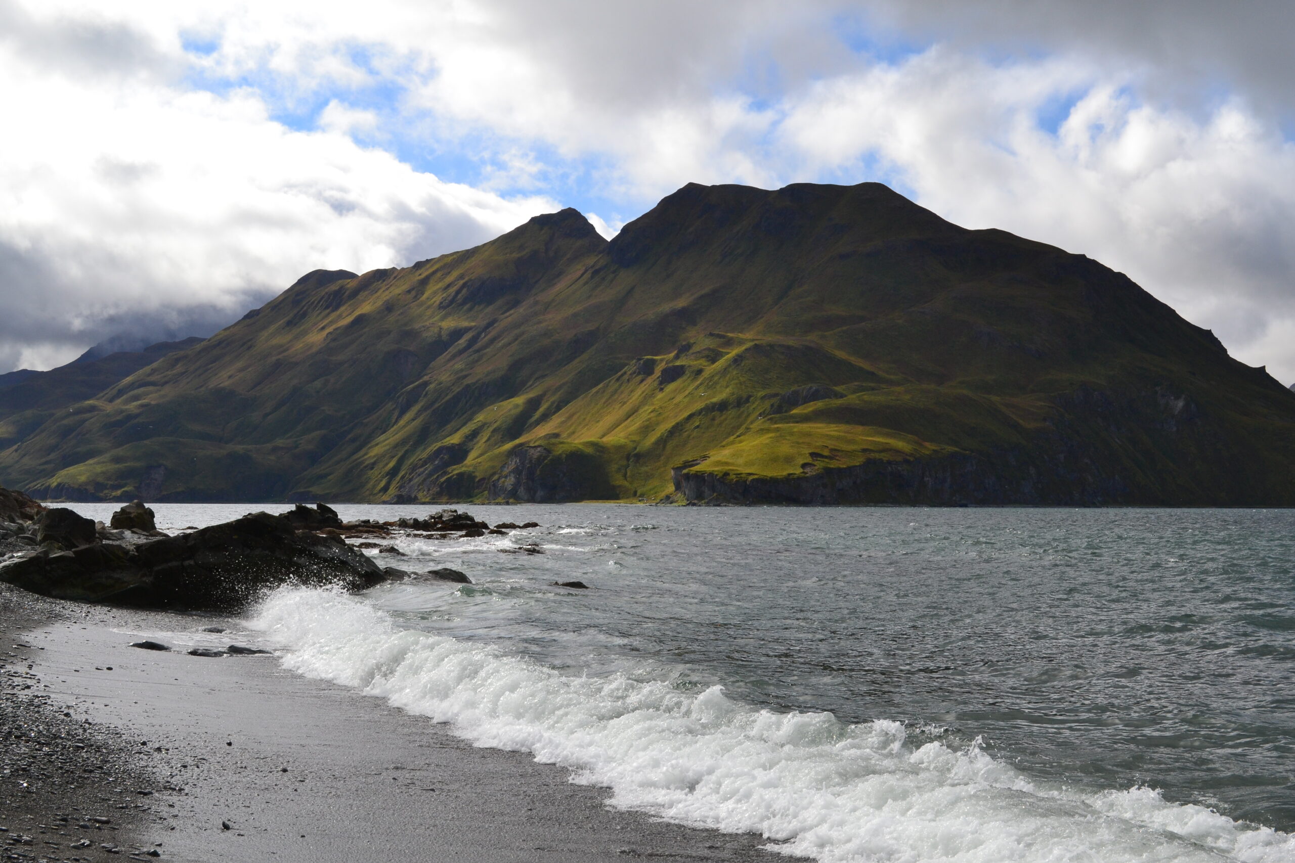 Beach with waves breaking on dark sand, mountain in the distance