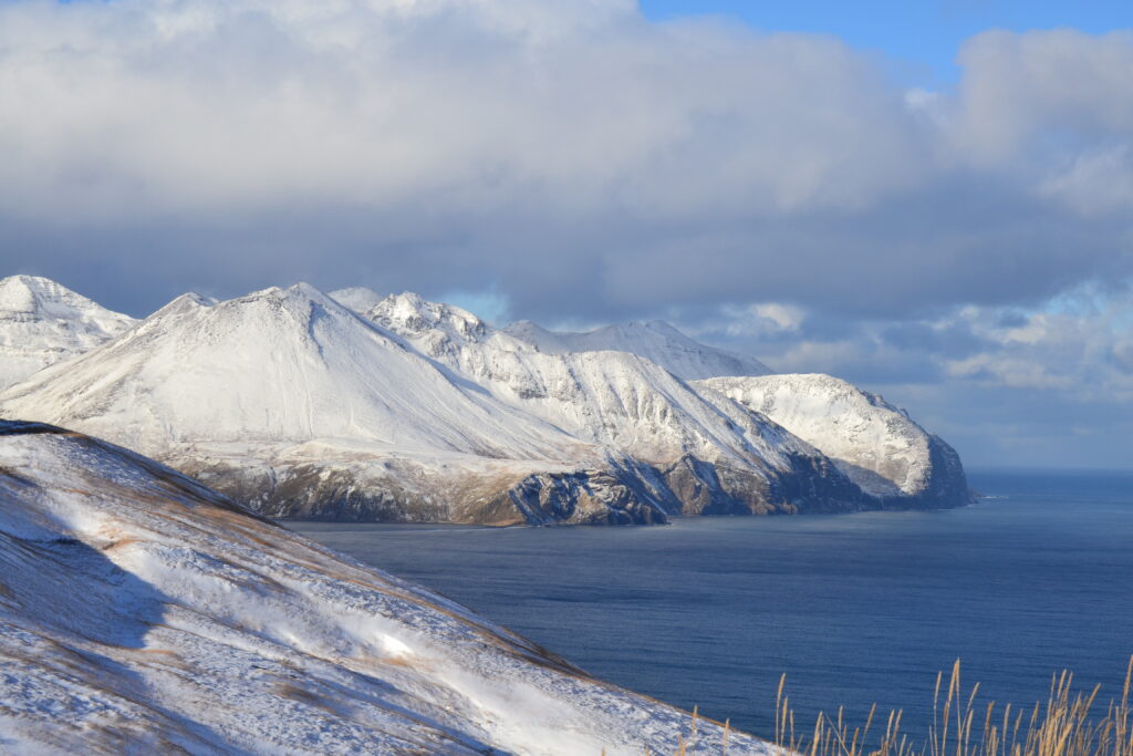 Snow covered peaks in Unalaska with cliffs coming out of ocean