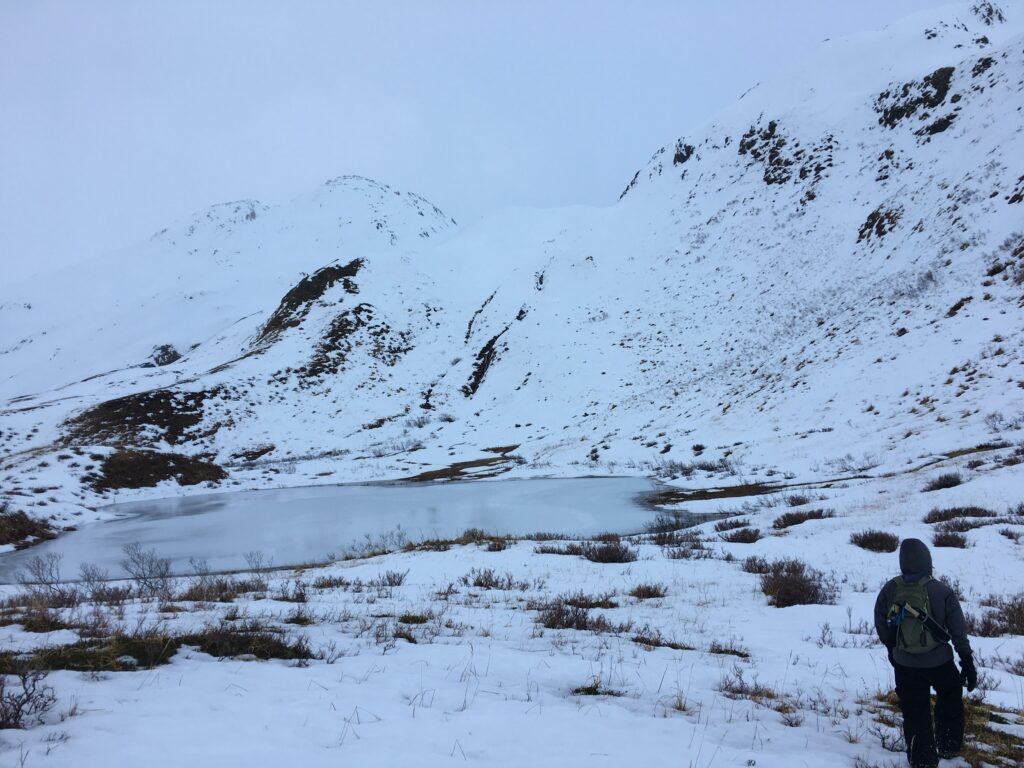 Man hiking up a snowy mountain passing by a frozen lake