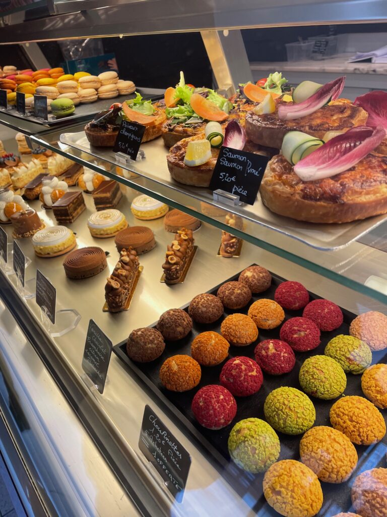 A display case at a french bakery with colorful french chouxs, tarts, and macarons