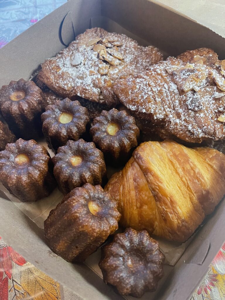 French pastry box full of almond croissants, butter croissants, and caneles