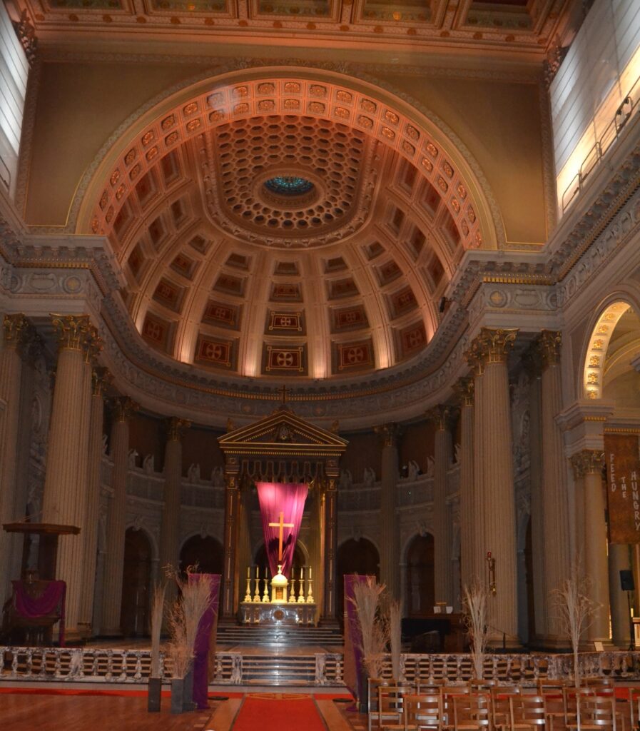 High altar of a Catholic Church flanked by two huge columns with a towering domed ceiling above