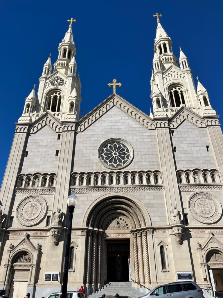 A church entrance surrounded by columns, above a rose window, two bell towers flank the edifice.