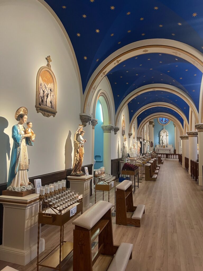 Statues of various Marian apparitions with votive candles and kneelers before each one.