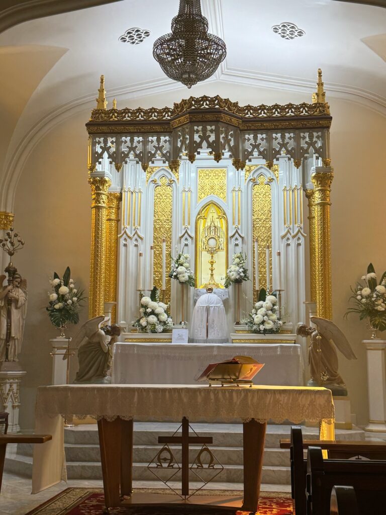 Gilded high altar with exposition of Blessed Sacrament surrounded by white flowers
