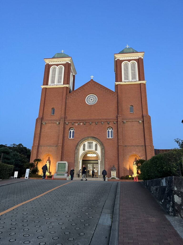 A road up a hill leads to the front of a red brick catholic church