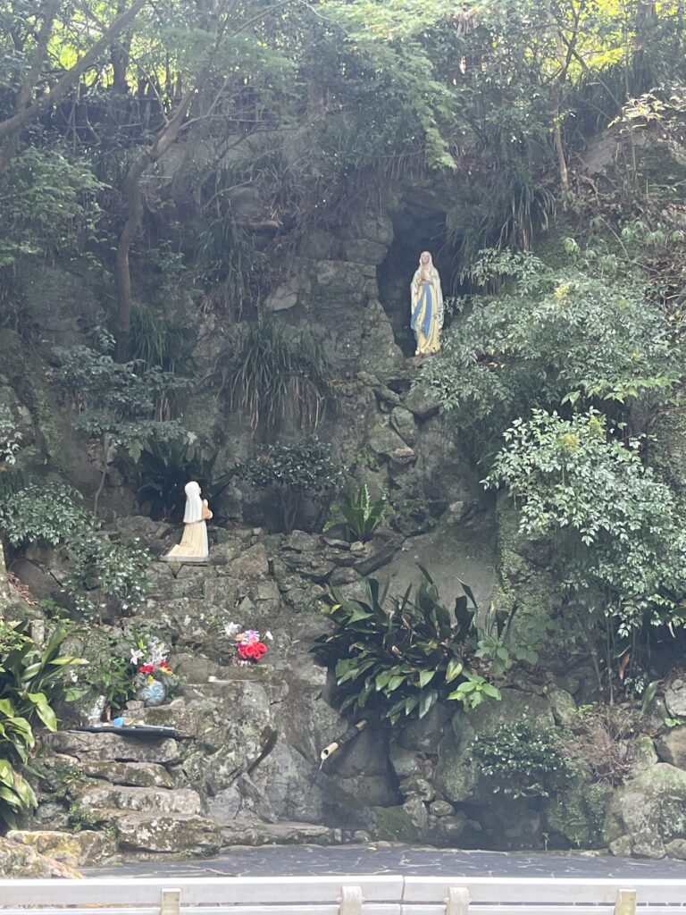 A rockface replicating the Lourdes grotto in France with statues of Mary in an alcove and St. Bernadette above a little stream