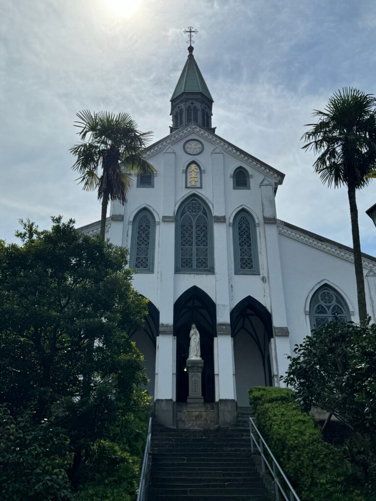 Stairs lead to a church flanked by two palm trees, with a statue of Mary at the top of the stairs.