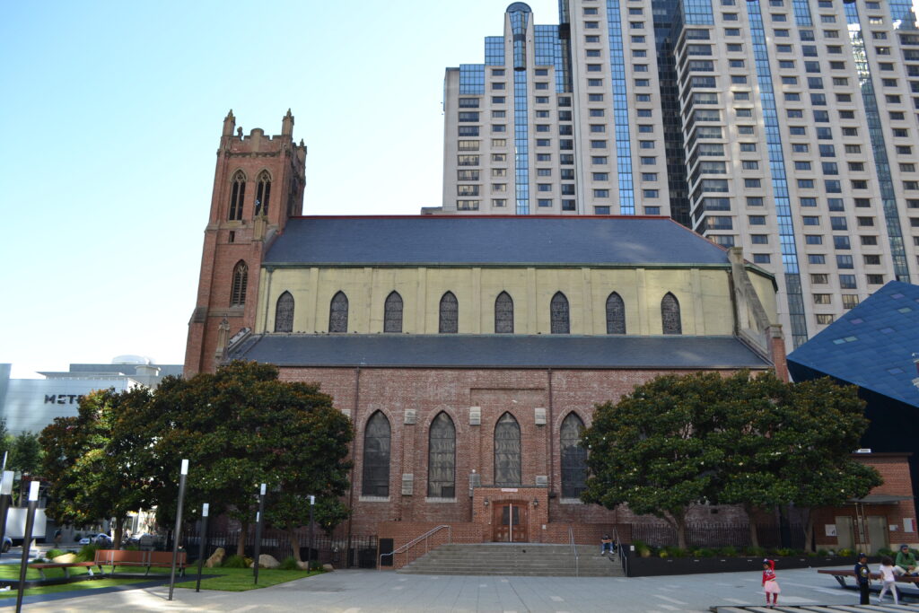 two magnolia trees flank the side of a brick church with high rise buildings in the back
