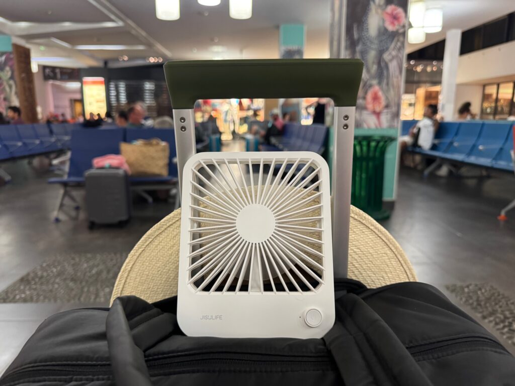 Personal fan on top of a duffle bag leaning against luggage handles in an airport