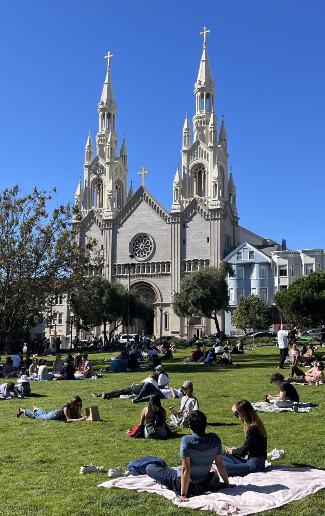 People lounging in a park with a Catholic Church in the background