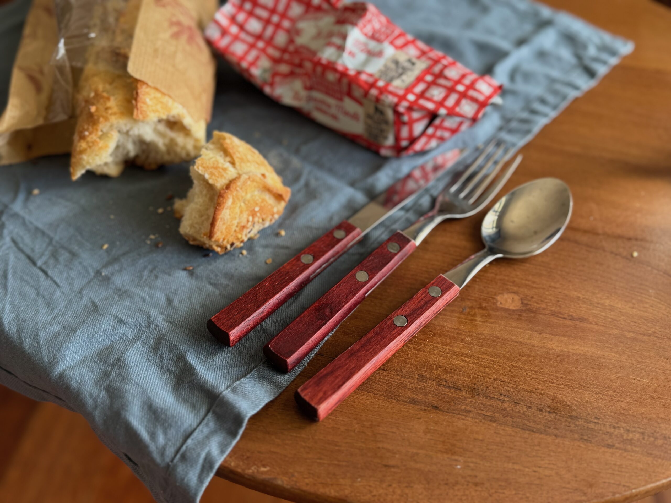 Set of cutlery with wooden handles on a table next to a baguette and french butter