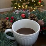 mug of hot chocolate surrounded by garland and in front of a Christmas tree