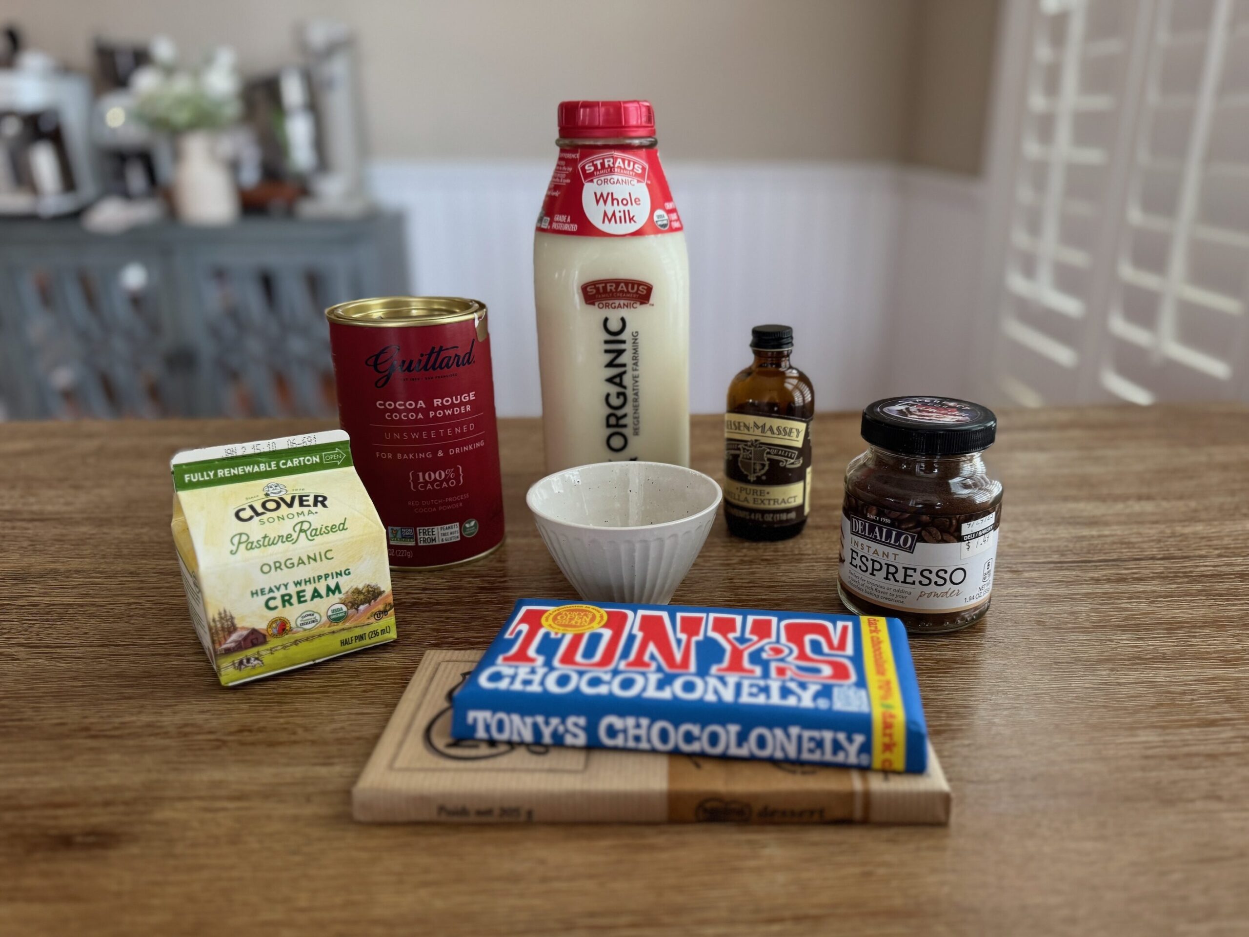 Ingredients on a table containing milk, vanilla, chocolate, cocoa powder, cream, and espresso powder