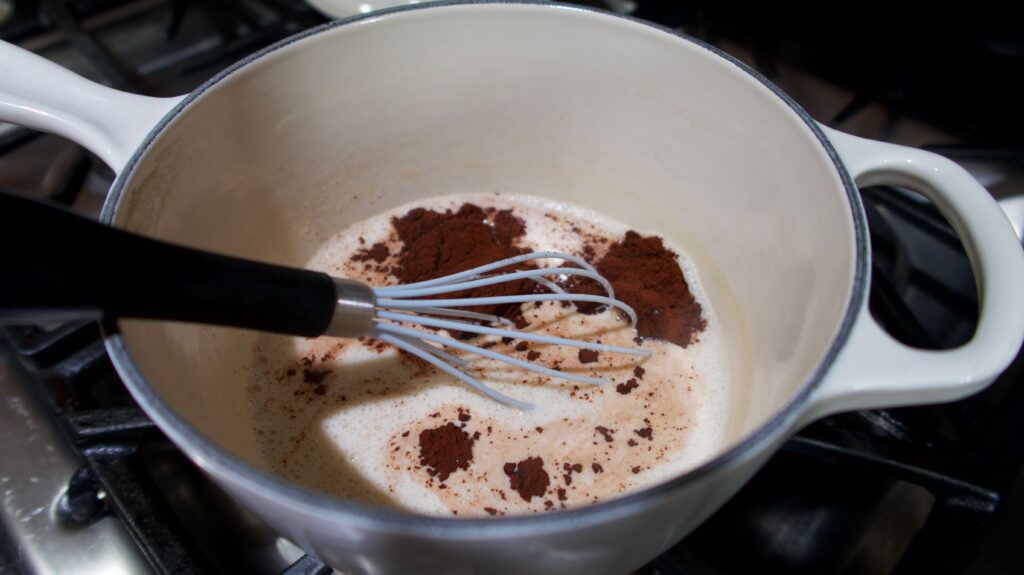 milk with cocoa powder in a saucepan over a stove with a whisk in the pan
