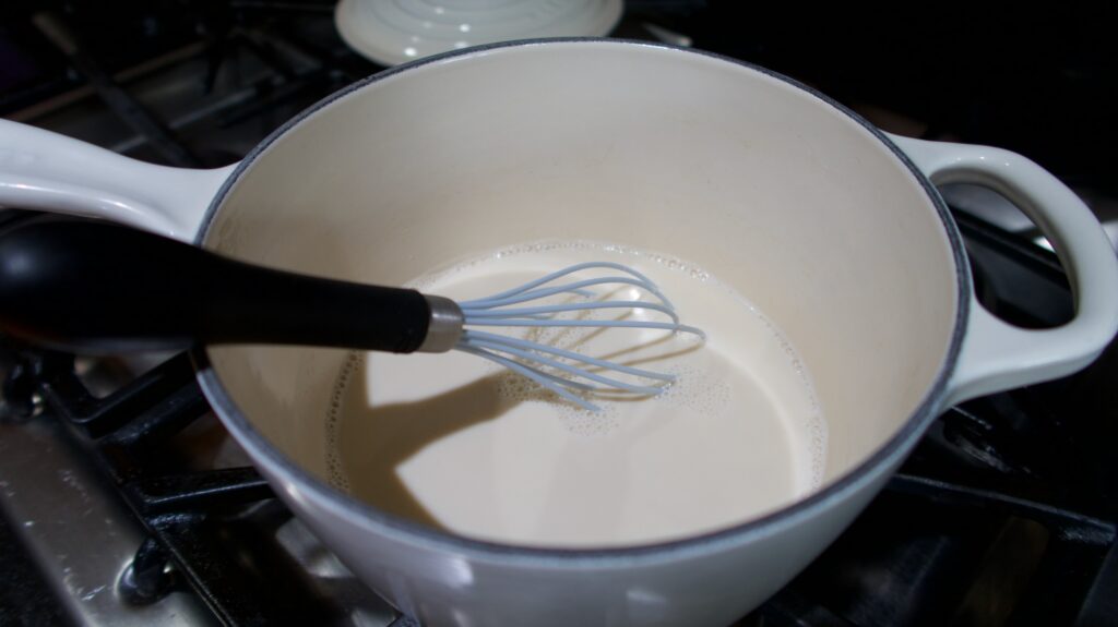 milk in a saucepan over a stove with a whisk in the pan being stirred