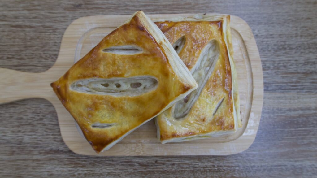 Two ham and cheese puff pastries on a cutting board