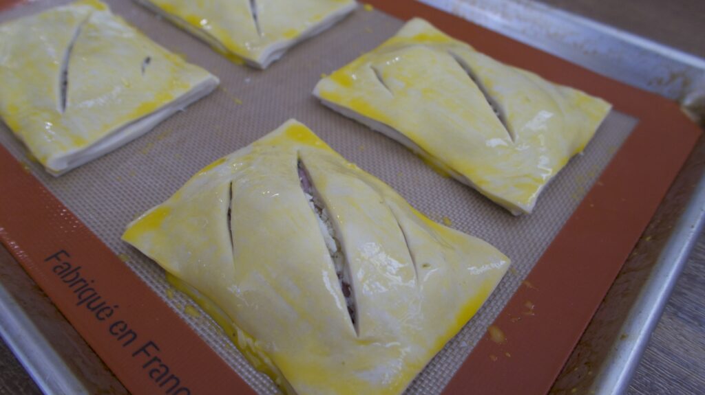 Puff pastries with egg wash on top on a baking tray
