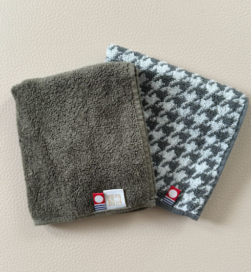 Two small folded towels laid flat on a table with a red logo tag on it