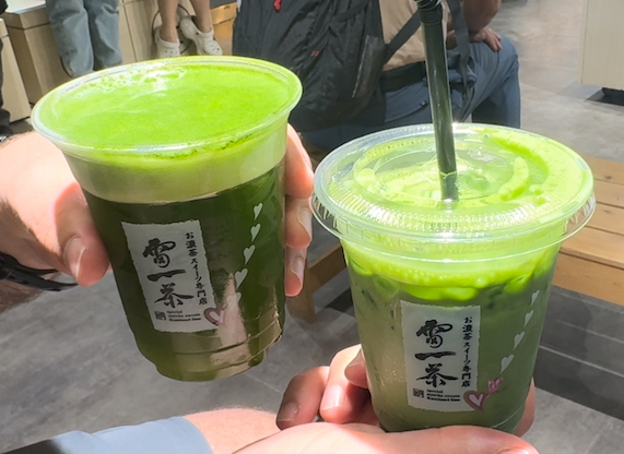 Hands holding two to-go cups of matcha drinks