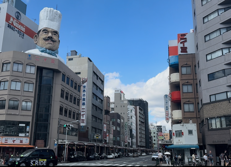 Corner of a street with teacups as balconies and a bust of a chef on top of a building