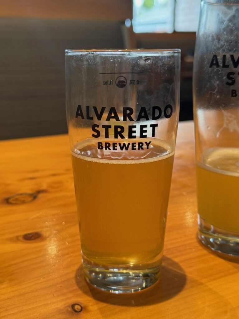 Glass of beer half drunken on table with Alvarado Street Brewery written on the glass