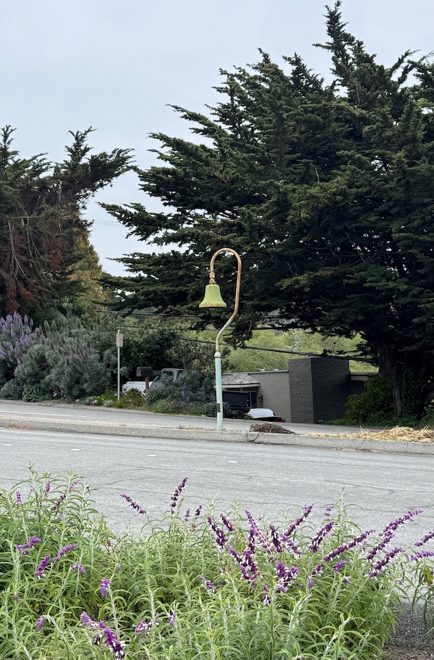 Roadside California Missions bell with cypresses in the background and purple flowers in the foreground.