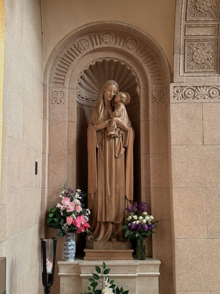 Stone statue of Our Lady holding baby Jesus in a stone alcove made of same stone material
