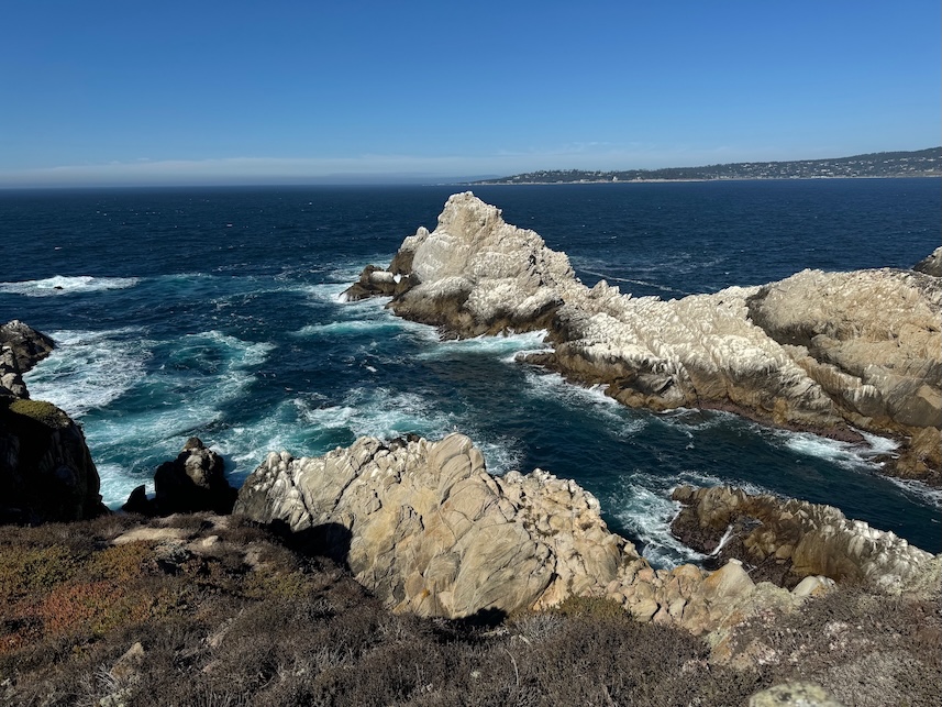 Rocky northern California coast with waves crashing against the rocks and blue ocean waters with a peninsula in the background