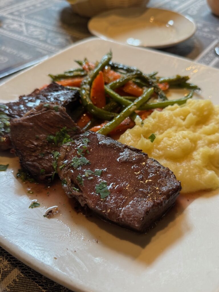 Plate of braised beef with mashed potatoes and side of green beans and carrots