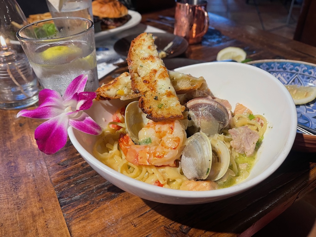 Bowl of seafood pasta garnished with slices of cheesy garlic bread and an orchid flower