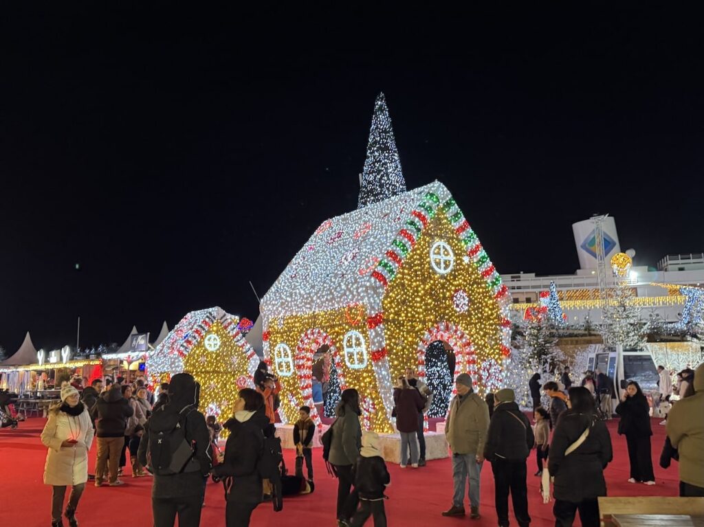 Life-sized gingerbread house made out of lights with a large crowd gathered in front