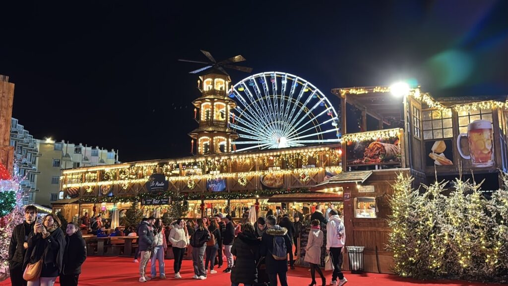 A two-story building light up with Christmas lights selling food with an illuminated ferris wheel in the background