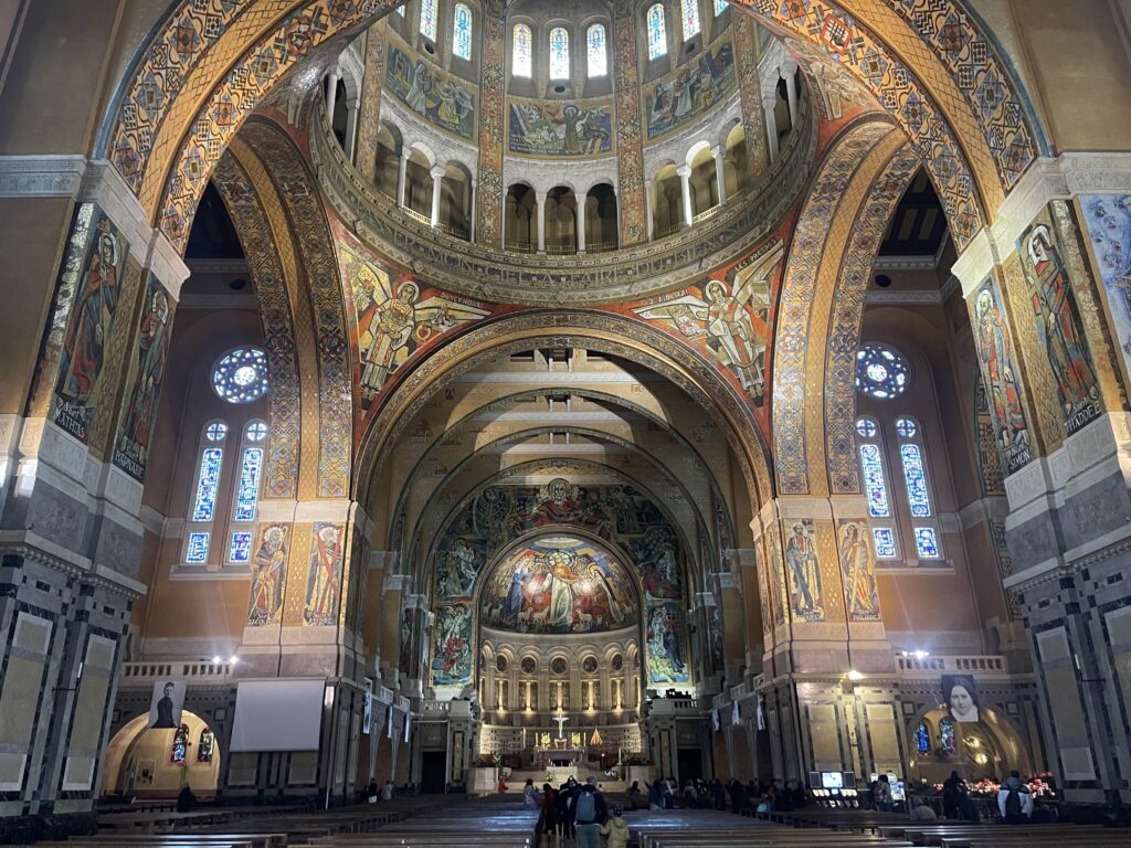 Interior of the basilica of St. Therese in France with towering dome ceilings covered in ornate mosaics on every surface