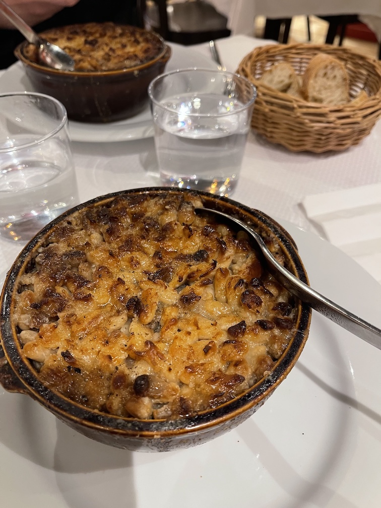 Two bowls of cassoulet on a table with a bread basket on the side
