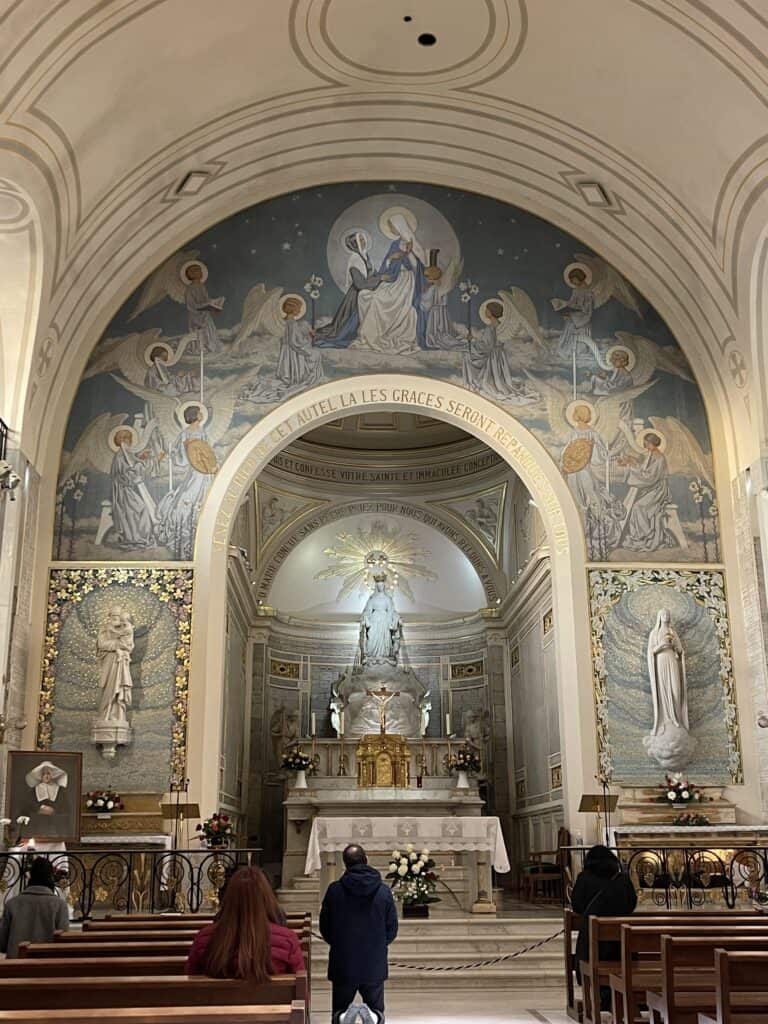 Altar of the Chapel of Our Lady of the Miraculous Medal with blue and white murals surrounding an altar with white statue of Our Lady and gold tabernacle with a crucifix on top