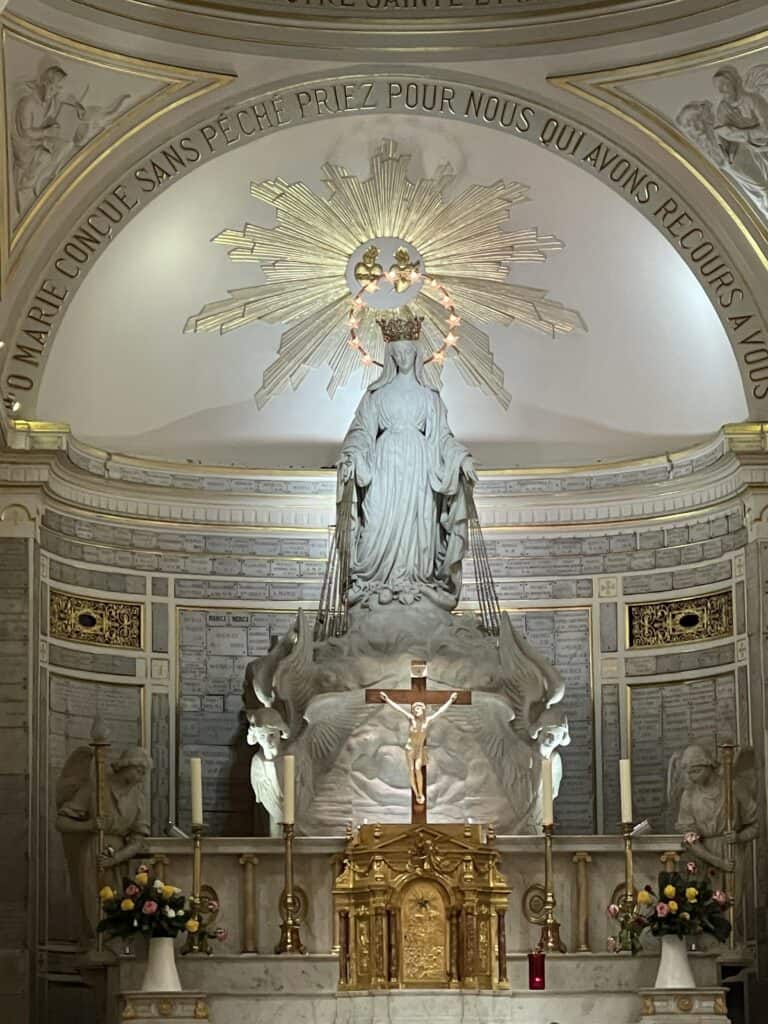 Altar at the Chapel of Our Lady of the Miraculous Medal in Paris, France with a beautiful white statue of Our Lady with a gold crown on the center and a golden tabernacle and crucifix on the altar
