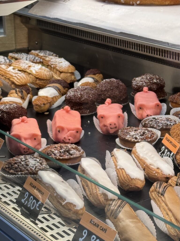 French pastries lined up in a display case with eclairs, tarts, and pig shaped desserts