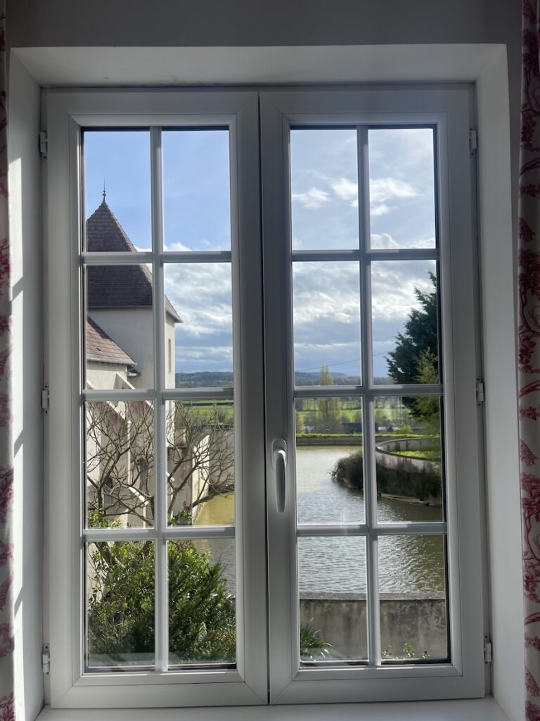 Picture taken through a window in the French countryside with a pond and normandy style house