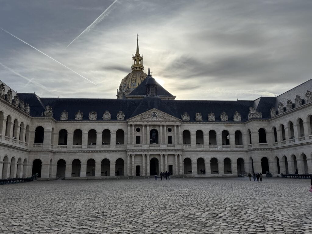 Courtyard view of the Invalides in Paris, France with a towering gold gilded dome behind the center of the building