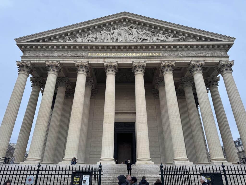 Entrance of La Madeleine in Paris, France with greek style architecture and towering columns. Relief sculpture of The Last Judgment above the main entrance.