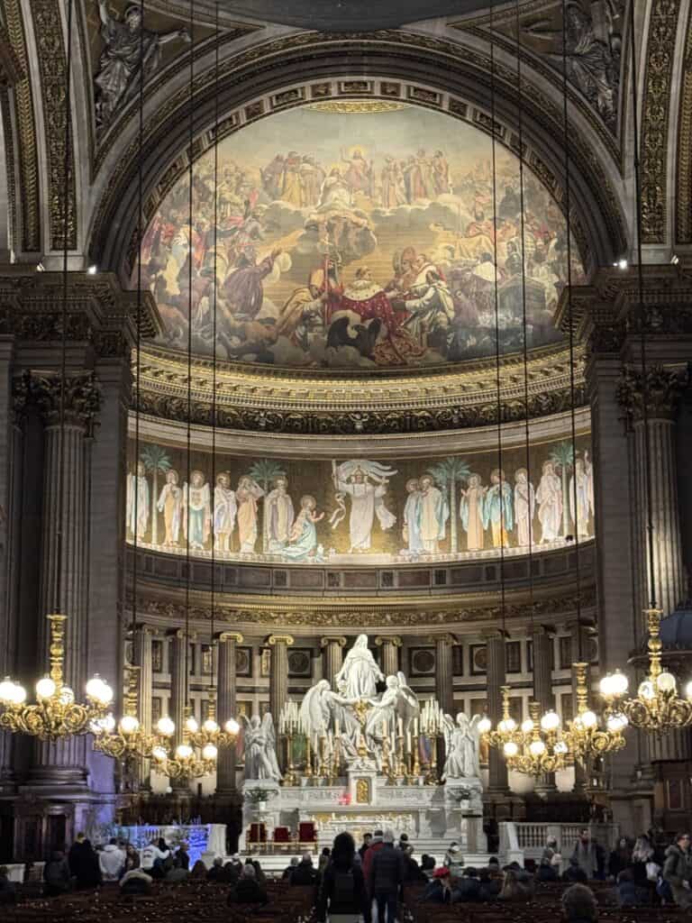 Interior and altar at La Madeleine church in Paris, France with beautiful intricate mosaics across the top with a huge statue of Mary standing over the altar with a tabernacle in the center