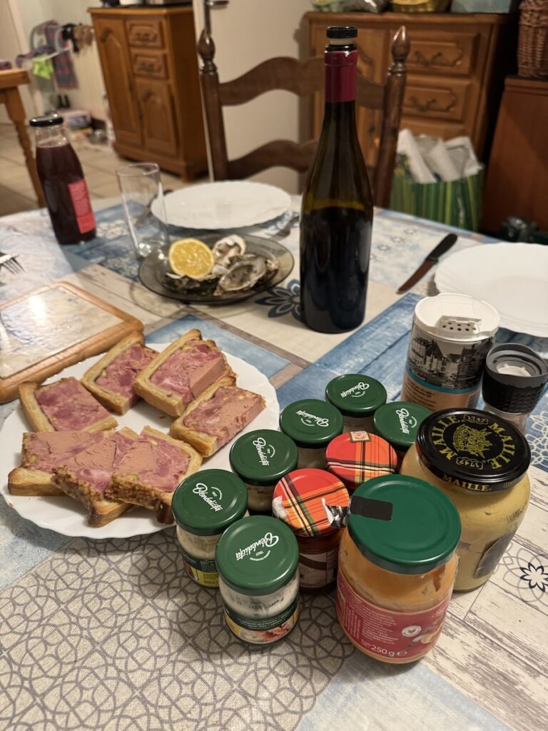 Dining table with pate en croute and jars of French sauces as well as a bottle of red wine and a plate of oysters