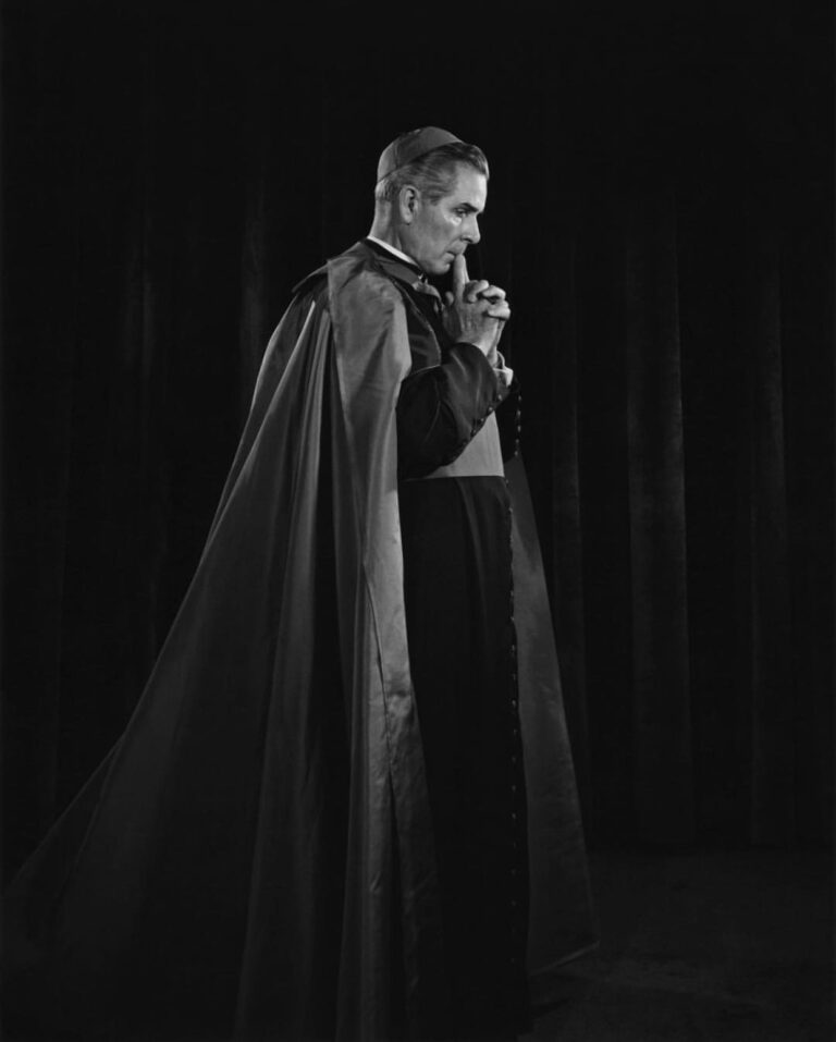 A black and white side profile photo of Archbishop Fulton J. Sheen in deep thought and prayer with his hands folded and held up to his chest. He is wearing his full clerical garb