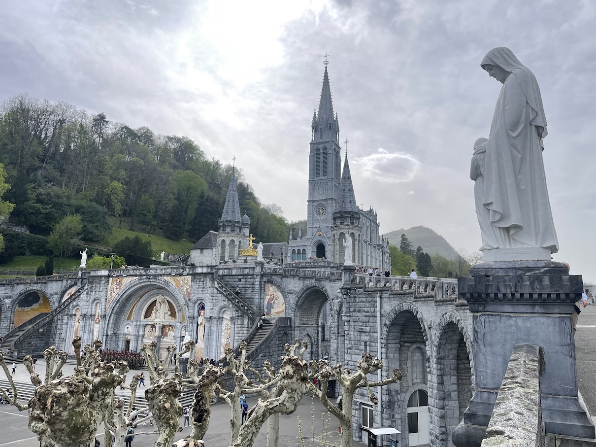 Picture of the basilica at the sanctuary of Lourdes taken from the side path leading up to the upper basilica. There's a statue of St. Anne on the side toward the front of the frame. This picture is horizontal version