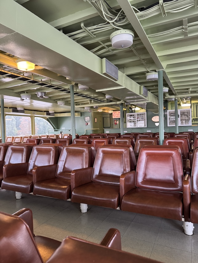 The interior of a ferry with rows of brown leather chairs and a light sage green interior paint