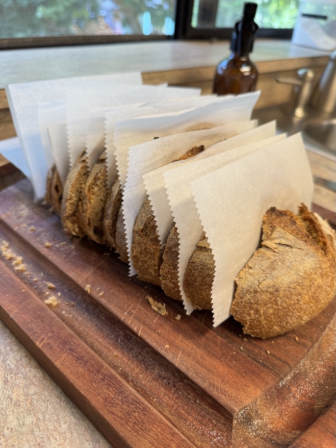 A loaf of bread on top of a wooden cutting board has been sliced up with parchment paper slid in between each slice before being put in the freezer.