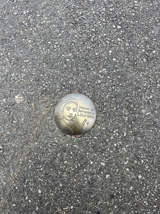 Metal markers indicating the route of St. Bernadette in Lourdes, France that are embedded onto the cement ground