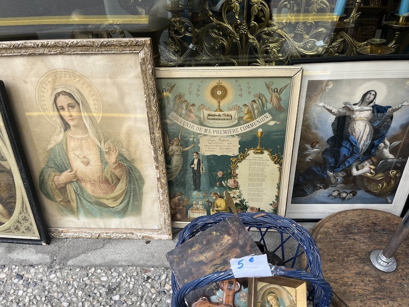 Vintage Catholic art being sold at the front of an store window with images of Our Lady in frames